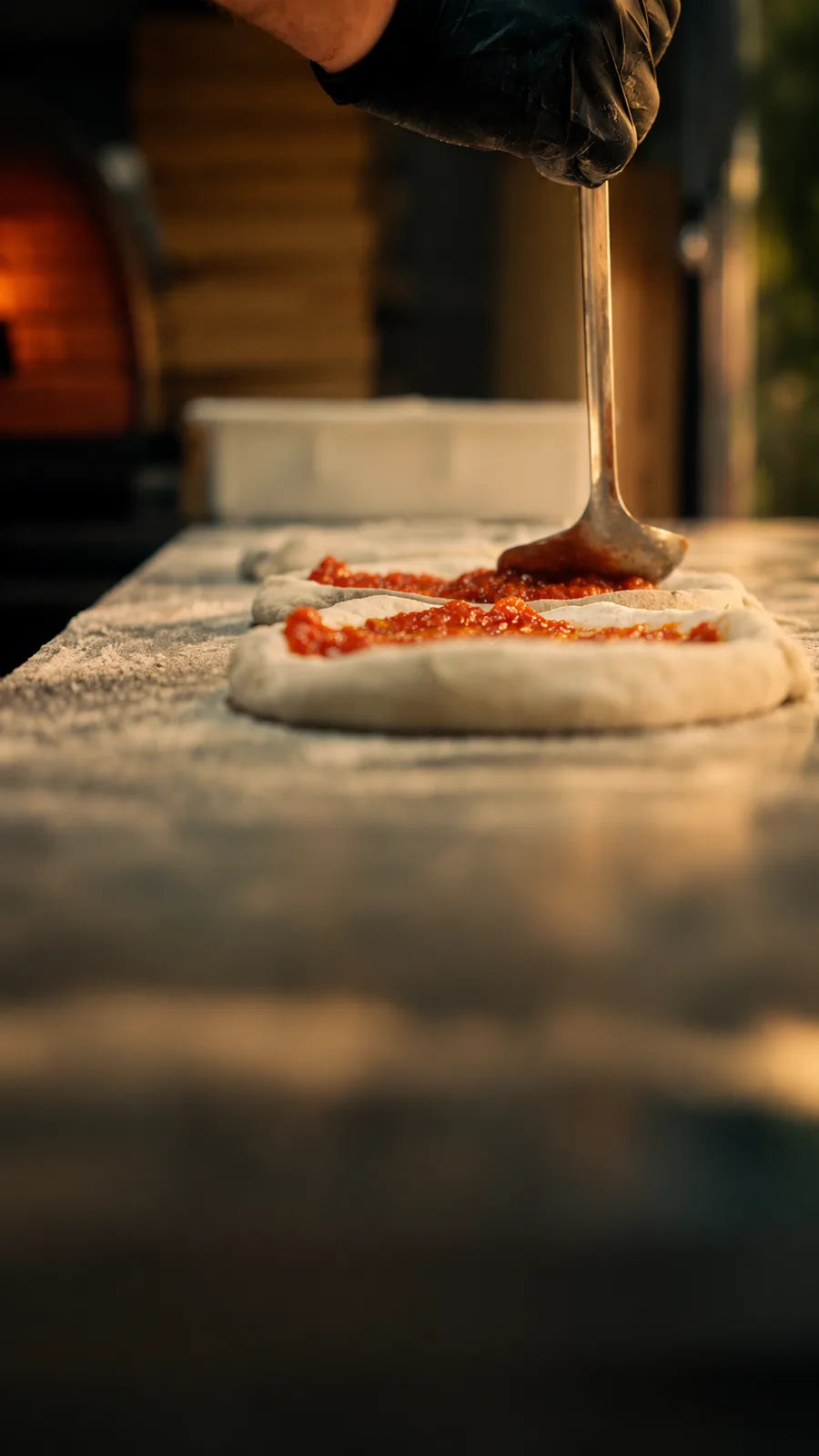 Sauce tomate étalée sur un pâton ORA, devant le four à bois